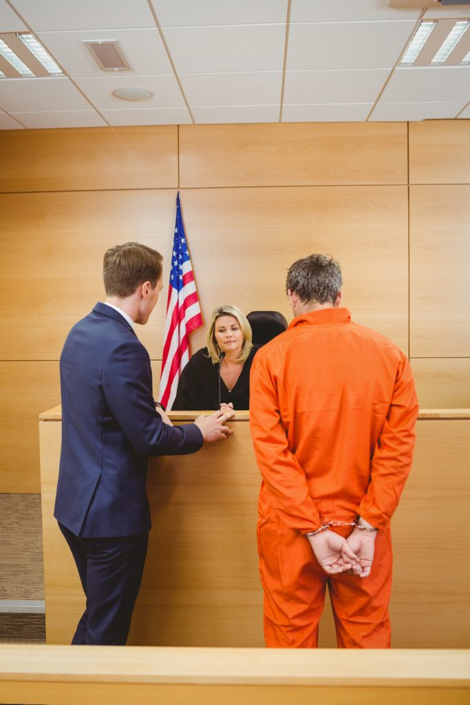 Lawyer and judge speaking next to the criminal in jumpsuit in the court room